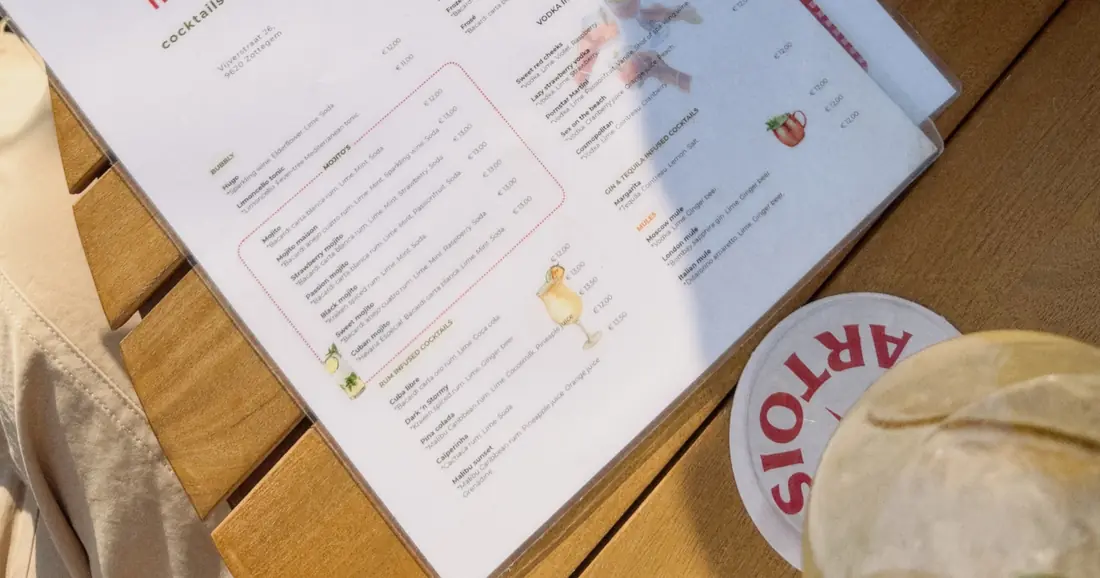 De drankkaart van De Zoeten Inval met cocktails en bites, naast een Stella Artois-viltje